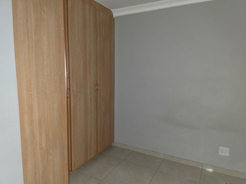 A vacant bedroom featuring light wood-finish built-in cupboards, neutral grey walls, and tiled flooring.