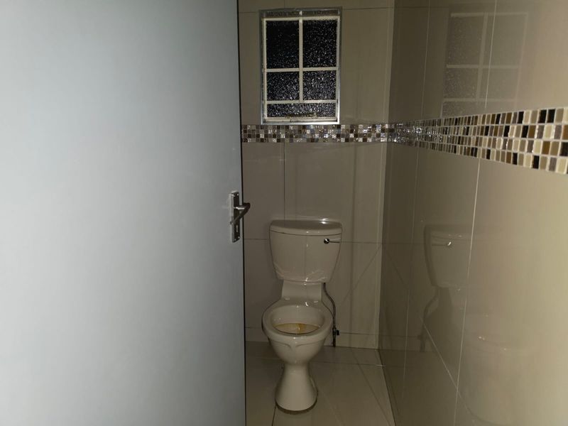 A compact guest bathroom featuring tiled walls with a decorative mosaic border, tiled flooring, and a small window with security bars.