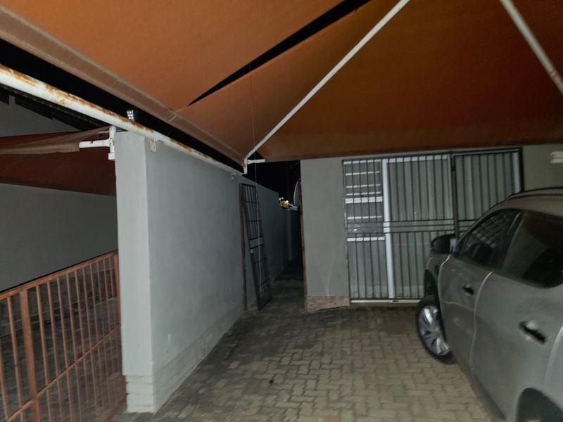 Covered parking area featuring a paved driveway, security gate, and a retractable awning showing signs of wear.