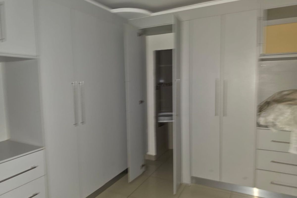 A clean, modern bedroom featuring extensive built-in cabinetry with sleek handles and neutral tiled flooring, offering ample storage space.
