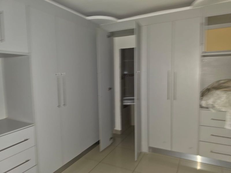 A clean, modern bedroom featuring extensive built-in cabinetry with sleek handles and neutral tiled flooring, offering ample storage space.