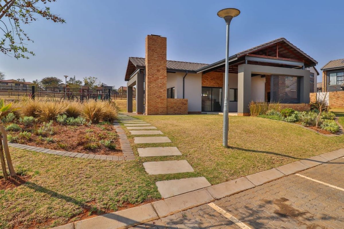 A well-maintained townhouse exterior featuring a brick chimney, covered patio area, and landscaped garden with a paved walkway.