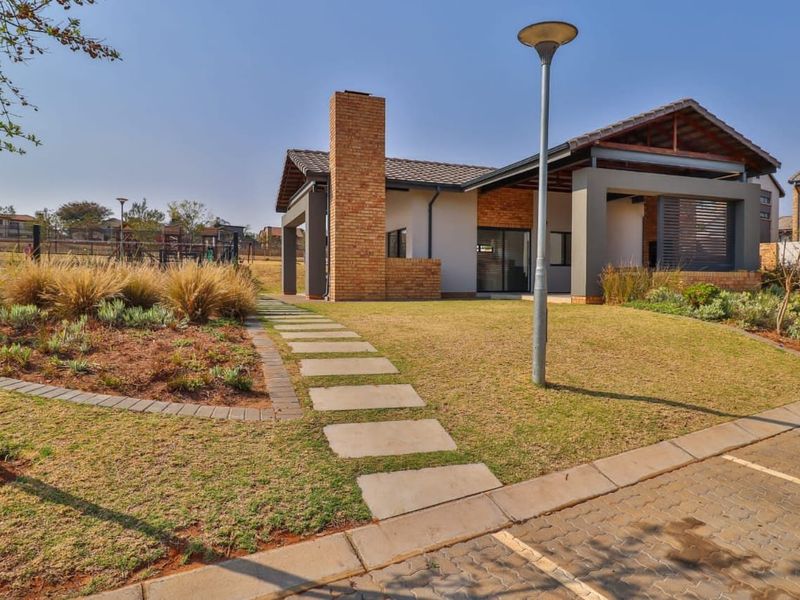 A well-maintained townhouse exterior featuring a brick chimney, covered patio area, and landscaped garden with a paved walkway.