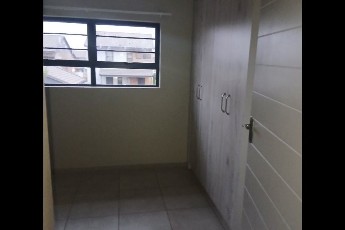 A bright, empty bedroom featuring neutral tiled flooring and modern built-in cupboards with light wood-grain finish.