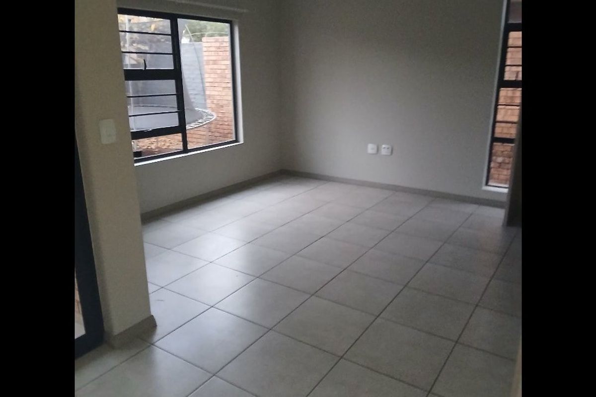 A bright, empty living room featuring neutral tiled flooring and large aluminium-framed windows, providing a clean and versatile space ready for furnishing.