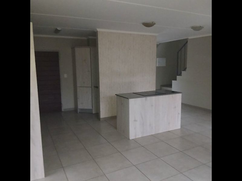An open-plan living area featuring a central kitchen island with a built-in hob, tiled flooring, and an internal staircase.