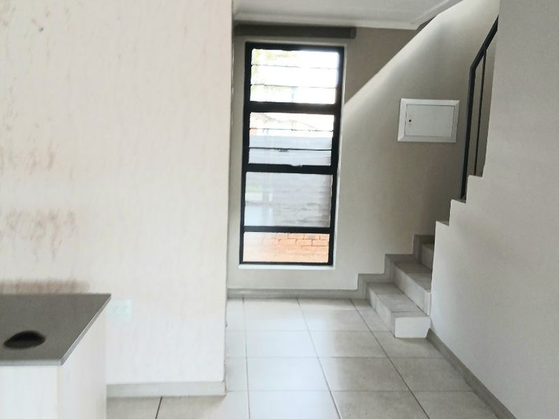 An open-plan living area featuring tiled flooring, a staircase with a metal balustrade, and a large window providing natural light.