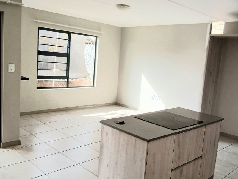 An open-plan living and kitchen area featuring a central island with a built-in hob, neutral tiled flooring, and ample natural light.