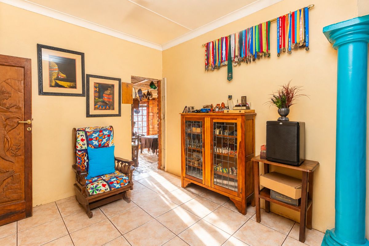 A living area featuring tiled flooring, coved ceilings, and a decorative column, providing access to an adjacent room.