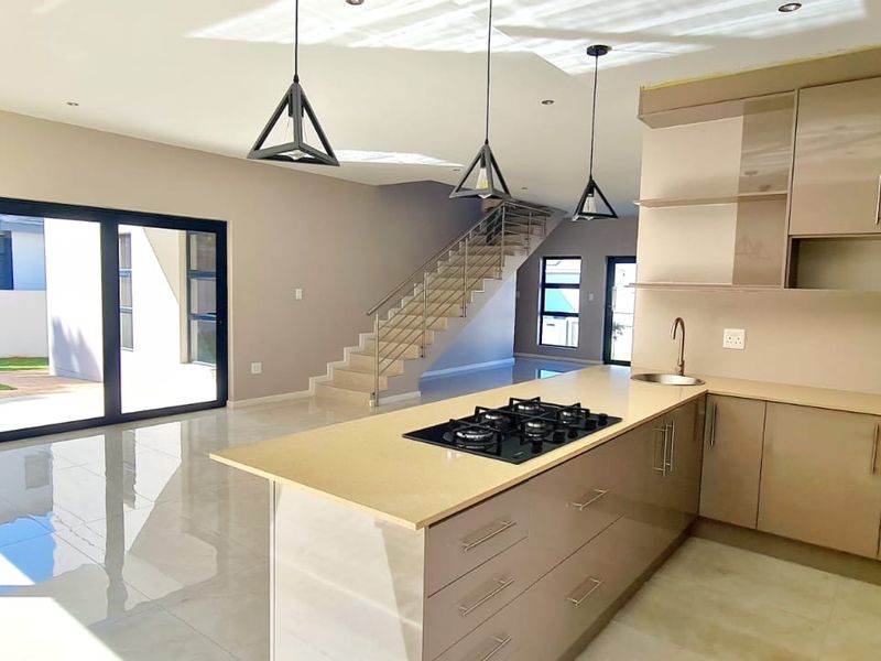 Modern open-plan living area featuring a sleek kitchen with gas hob, island, and seamless flow to the outdoor patio through large sliding glass doors.