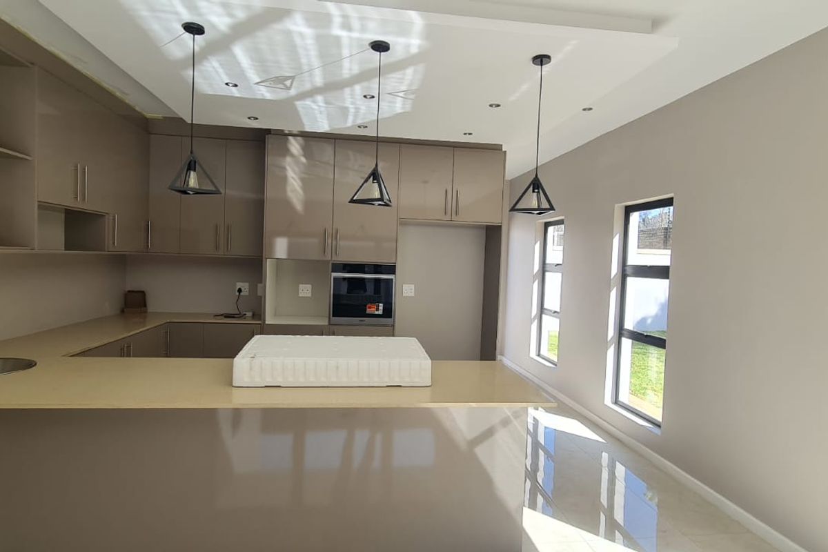 Modern kitchen featuring sleek high-gloss cabinetry, stone countertops, built-in oven, and contemporary pendant lighting in an open-plan layout.