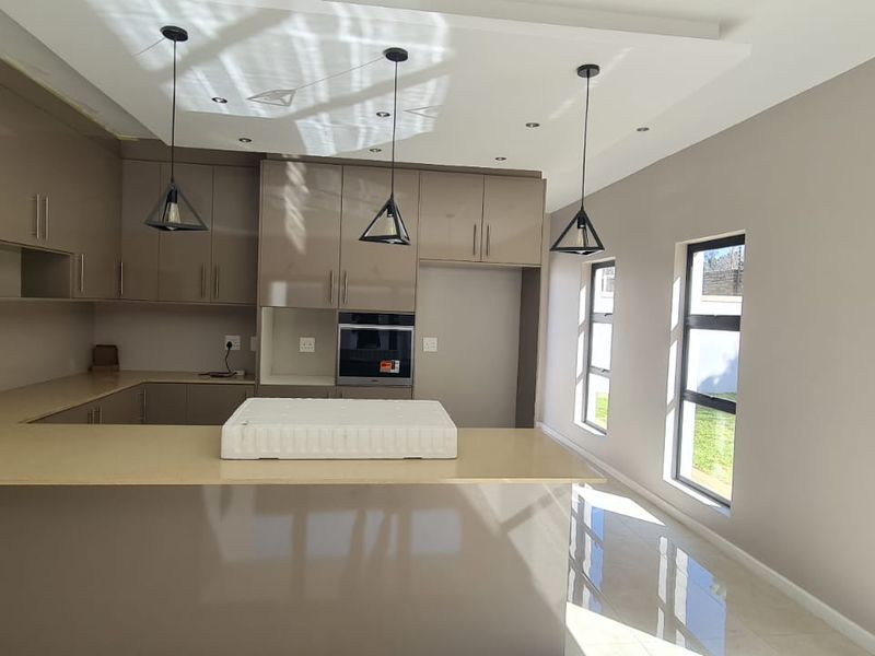 Modern kitchen featuring sleek high-gloss cabinetry, stone countertops, built-in oven, and contemporary pendant lighting in an open-plan layout.