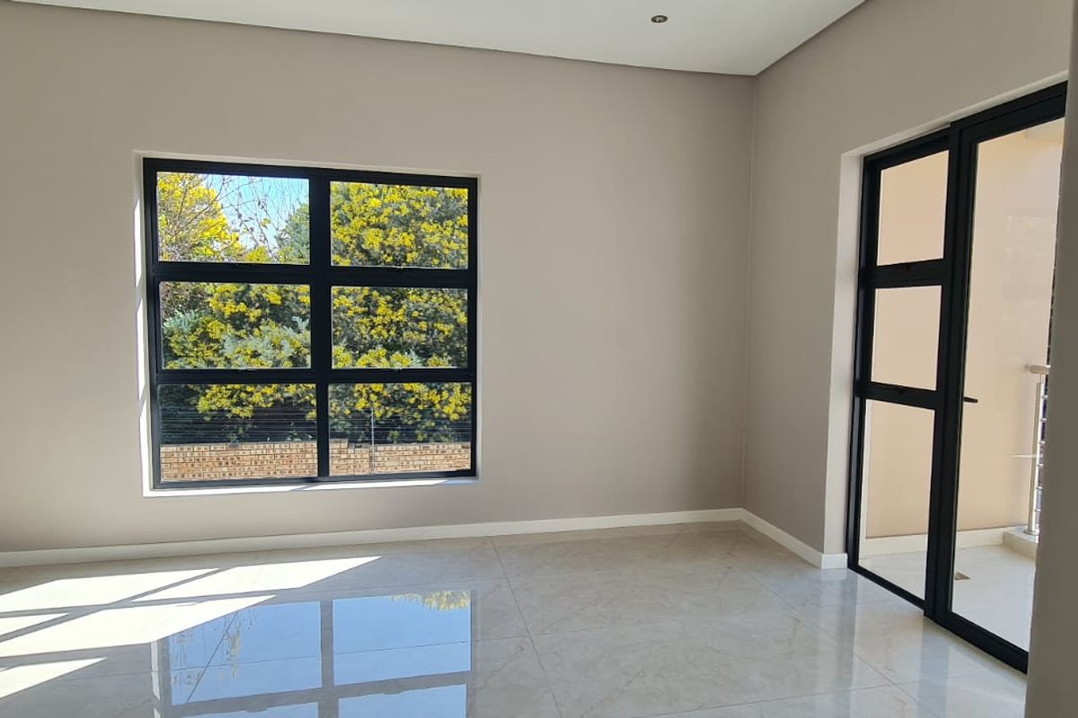 A bright, empty living area featuring modern tiled flooring, large aluminium-framed windows, and a sliding door providing access to an outdoor space.