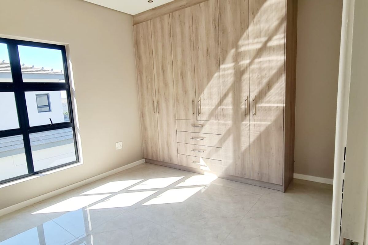 A bright, modern bedroom featuring neutral tiled flooring and extensive built-in wooden cabinetry, offering ample storage space and natural light.