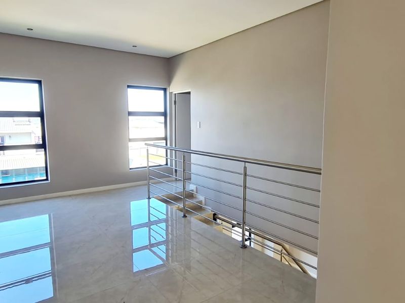 A spacious, modern landing area featuring polished tiled floors, neutral walls, and a sleek stainless steel balustrade overlooking the staircase.