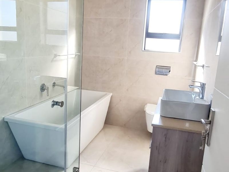 Modern bathroom featuring a freestanding bathtub, glass-enclosed shower, vessel sink on a vanity cabinet, and neutral floor-to-ceiling tiling.