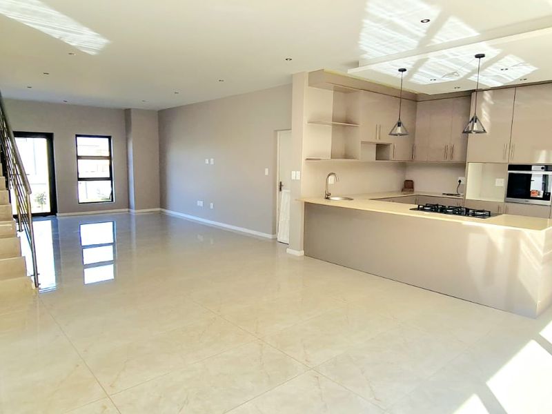 Spacious open-plan living area featuring a modern kitchen with built-in appliances, sleek cabinetry, and a staircase leading to the upper level.