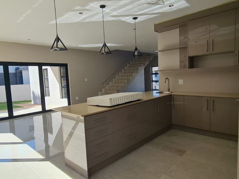 Modern open-plan living area featuring a sleek kitchen with stone countertops, tiled floors, and a staircase with a glass balustrade leading to the upper level.