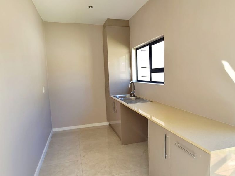 A clean, modern laundry room featuring sleek built-in cabinetry, stone countertops, a stainless steel sink, and large format floor tiles.