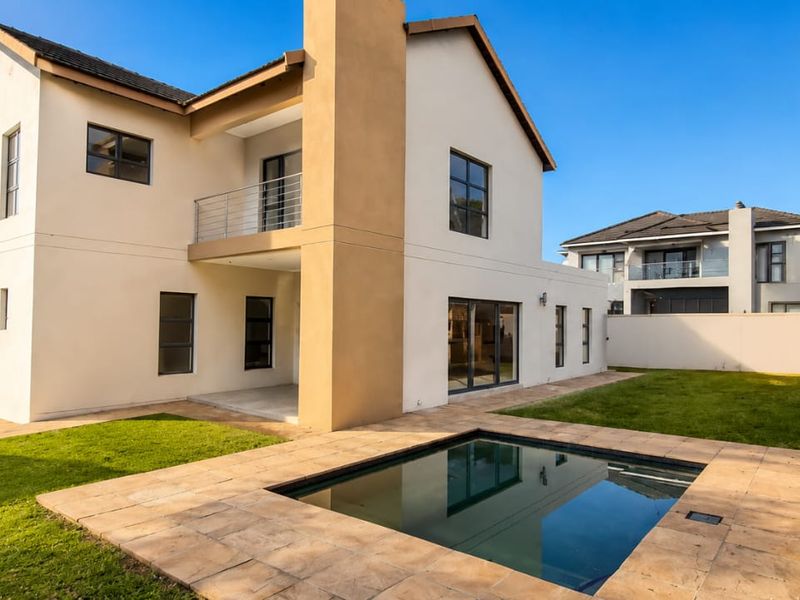 Rear view of a modern two-story house featuring a swimming pool, stone patio area, upper-level balcony, and a well-maintained garden.