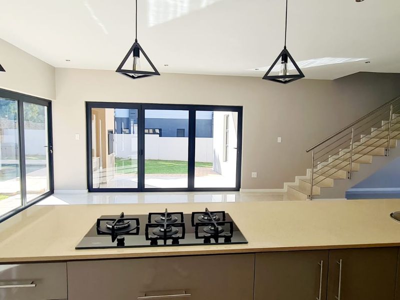 Modern open-plan kitchen and living area featuring a central island with gas hob, sleek cabinetry, and large sliding doors opening to the garden.