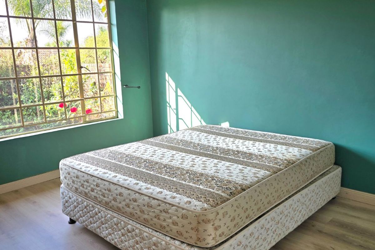 A bright bedroom featuring laminate flooring, green painted walls, and a large grid-pattern window allowing for natural light.