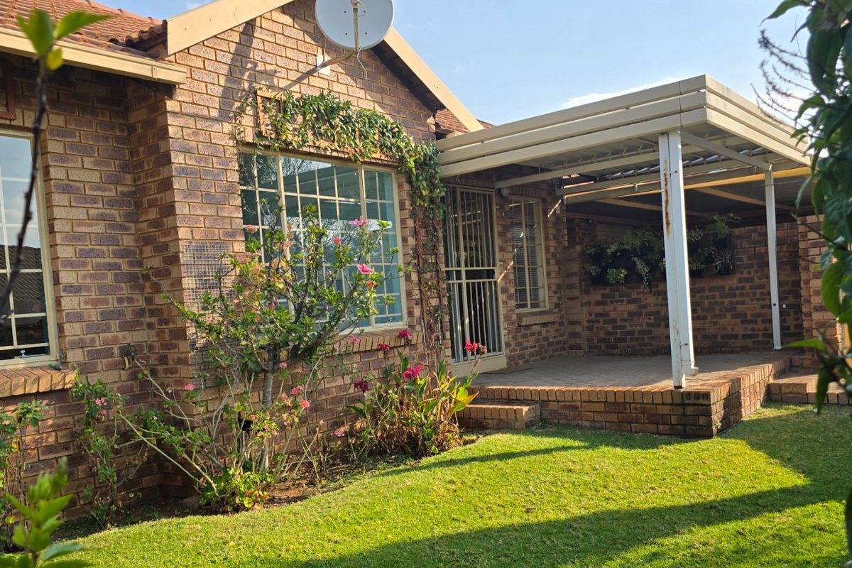 Rear view of the townhouse featuring a face-brick facade, a covered patio area with paved flooring, and a well-maintained garden.