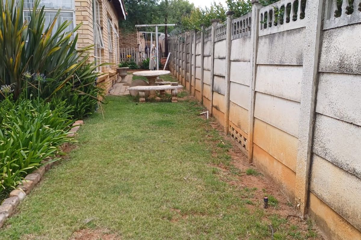 A side garden area featuring a lawn, paved walkway, and a precast concrete boundary wall.