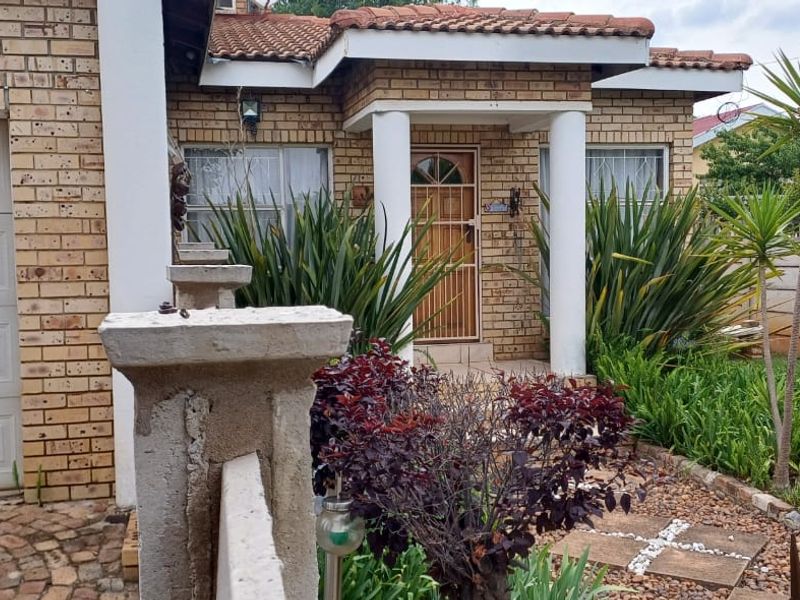 Front elevation of a face brick townhouse featuring a single garage, covered entrance porch with concrete columns, and a landscaped front garden area.