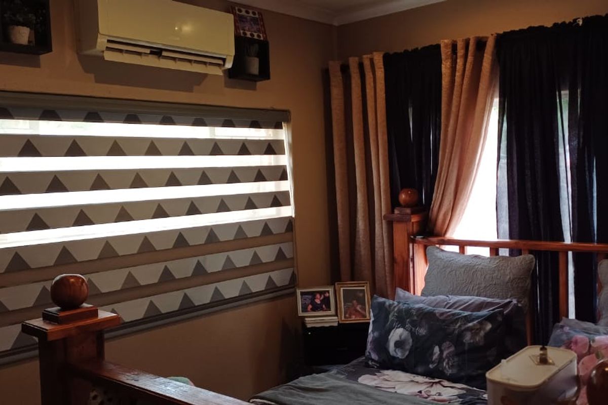 A bedroom featuring a split-system air conditioner, patterned roller blinds, and a timber balustrade, providing a functional and cozy living space.