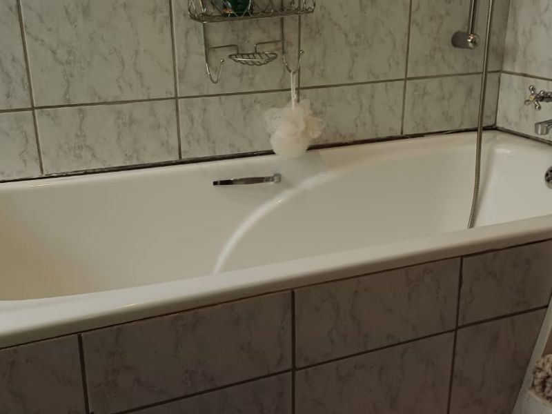 A functional bathroom featuring a built-in bathtub with wall-mounted shower mixer and tiled surround.
