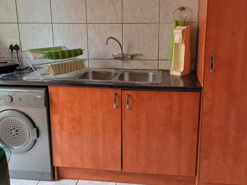 Functional laundry area featuring a double basin sink, tiled backsplash, laminate cabinetry, and dedicated space for a washing machine.