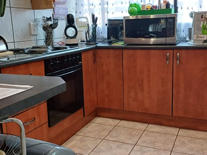 A functional kitchen featuring wood-look laminate cabinetry, dark countertops, built-in oven, electric hob, and tiled flooring and walls.