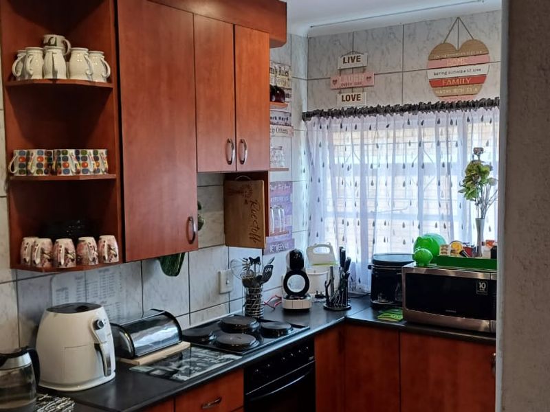 A functional kitchen featuring wooden cabinetry, dark countertops, an electric hob, and a tiled backsplash, offering a practical layout for daily meal preparation.