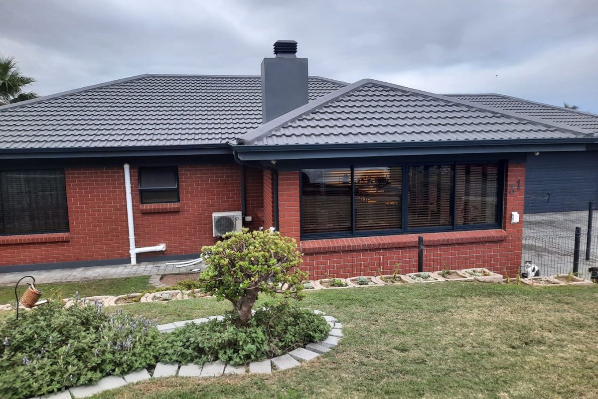Rear view of a well-maintained brick house featuring a dark tiled roof, chimney, and modern dark-framed windows overlooking a landscaped garden.