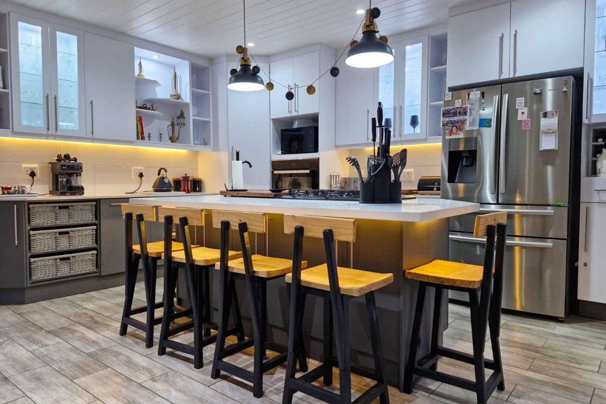 Modern kitchen featuring a central island with breakfast bar seating, quartz countertops, integrated appliances, and stylish under-cabinet lighting.