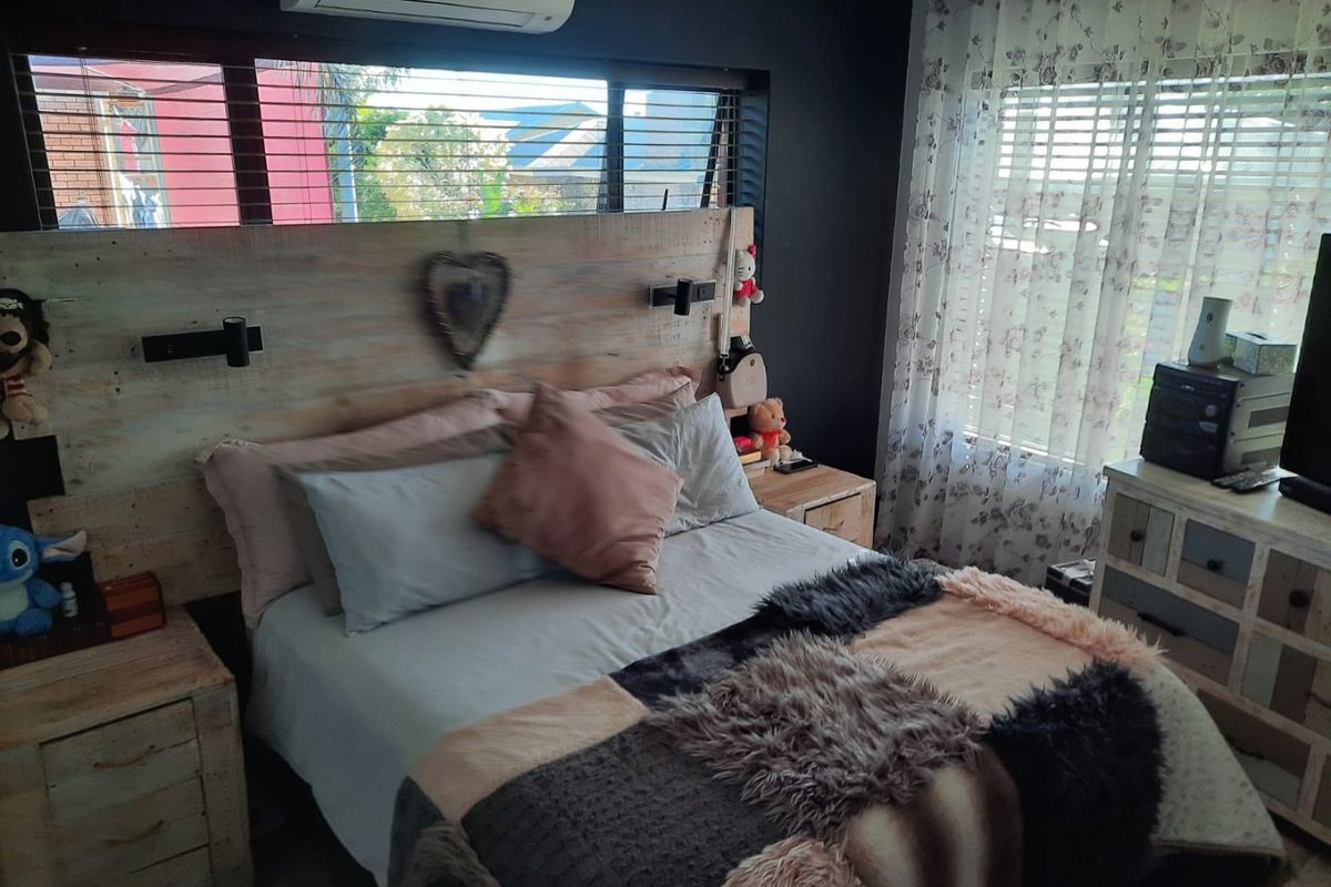 A bedroom featuring a built-in wooden headboard, split-system air conditioning, and horizontal window blinds.