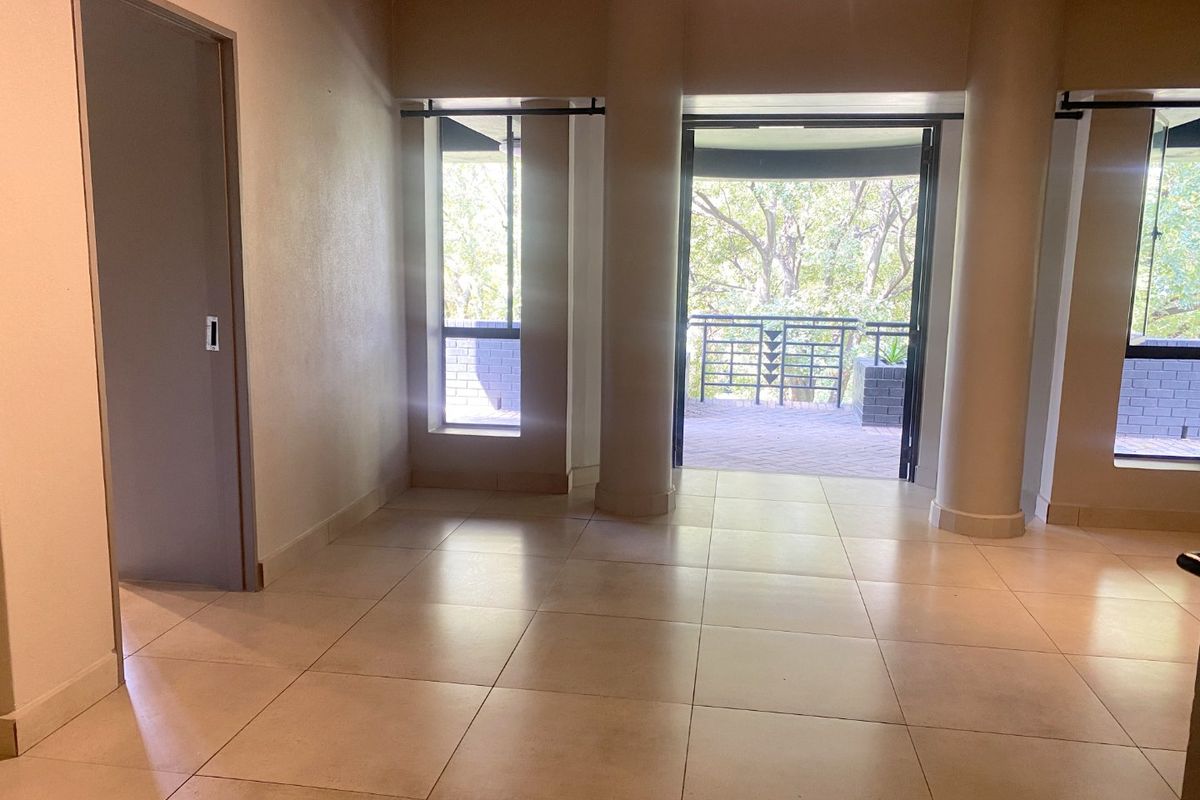 Spacious, empty living area featuring large structural columns, neutral tiled flooring, and direct access to an outdoor balcony through sliding doors.