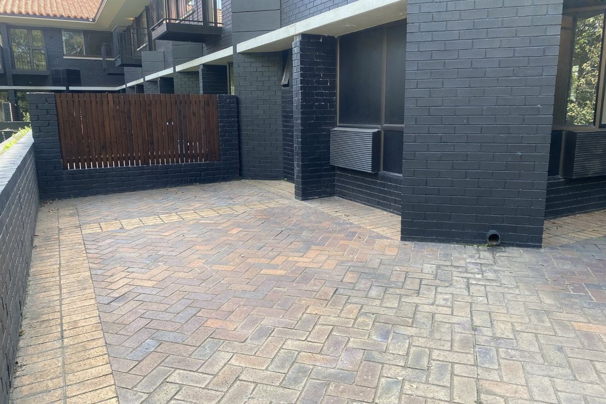 A private rear courtyard featuring herringbone brick paving, a painted dark brick facade, and a timber privacy screen.