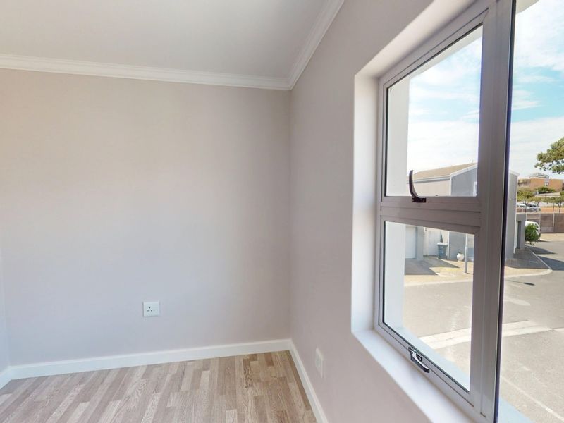 A bright, empty bedroom featuring neutral walls, laminate flooring, and a large aluminium window with a view of the street.