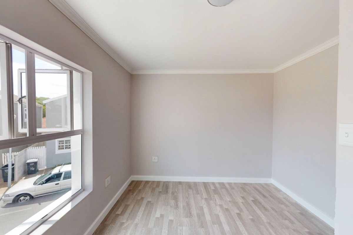 A bright, empty bedroom featuring neutral wall tones, modern laminate flooring, and a large window providing natural light.