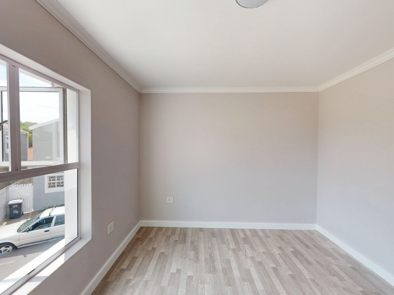 A bright, empty bedroom featuring neutral wall tones, modern laminate flooring, and a large window providing natural light.