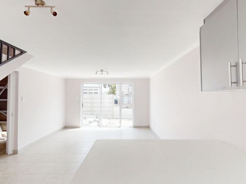 Bright open-plan living area featuring tiled floors, a staircase, and direct access to the rear exterior through sliding glass doors.