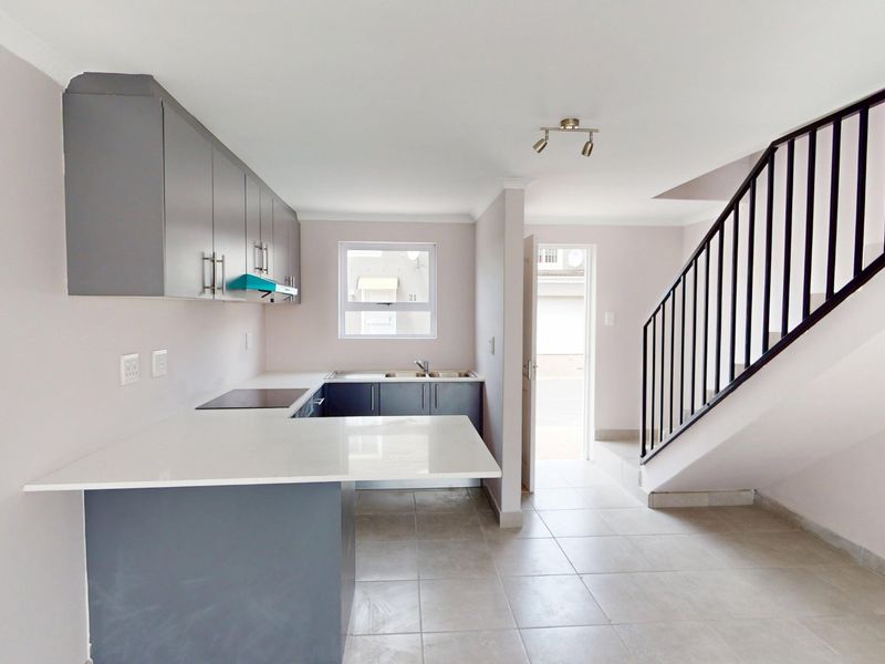 Modern open-plan kitchen featuring sleek grey cabinetry, stone countertops, and an integrated hob, adjacent to a staircase with a contemporary metal balustrade.