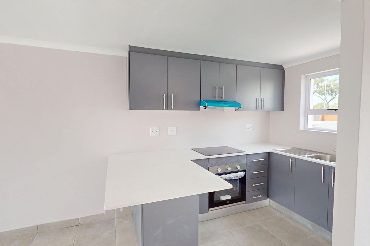 Modern kitchen featuring grey cabinetry, white stone countertops, built-in oven, electric hob, extractor fan, and stainless steel sink with tiled flooring.