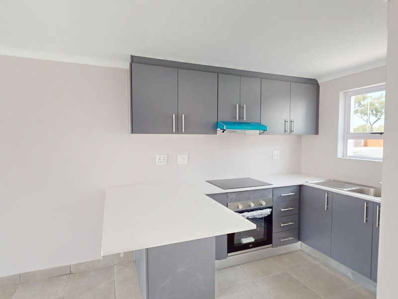 Modern kitchen featuring grey cabinetry, white stone countertops, built-in oven, electric hob, extractor fan, and stainless steel sink with tiled flooring.