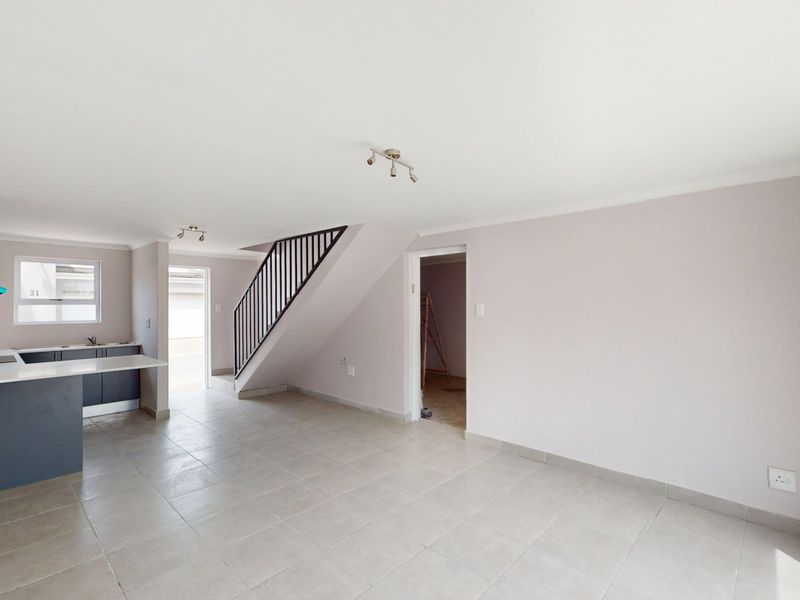 Spacious open-plan living area featuring a modern kitchen with stone countertops, tiled flooring, and a staircase with a sleek metal balustrade.