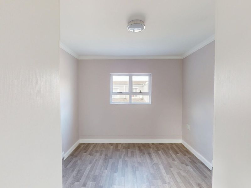 A clean, empty bedroom featuring neutral wall tones, modern laminate flooring, and a central ceiling light fixture.