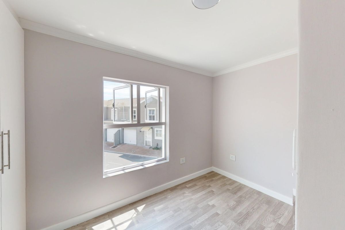 A bright, empty bedroom featuring neutral walls, laminate flooring, and built-in cupboards, offering a clean and versatile space.