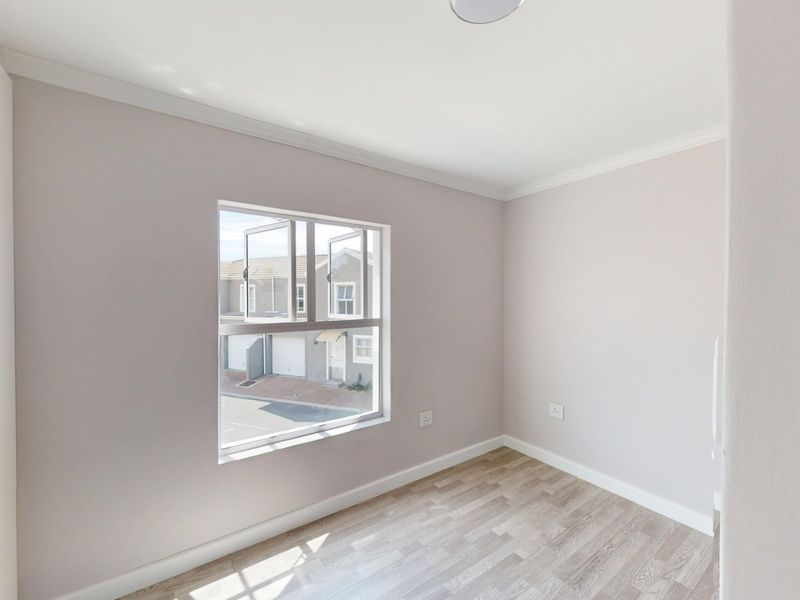 A bright, empty bedroom featuring neutral walls, laminate flooring, and built-in cupboards, offering a clean and versatile space.